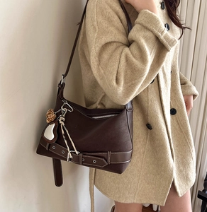 Detail of dark brown tote bag featuring silver eyelet belt strap and decorative charms