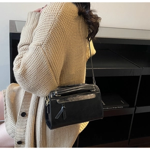 Détail d'un sac à bandoulière minimaliste en cuir noir avec bordure argentée et un pompon