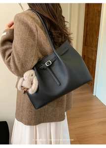 Detail of a black pebbled leather tote bag with buckle strap and a plush rabbit charm
