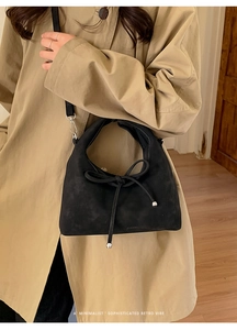 Close-up of black suede crossbody bag featuring unique ribbon tie and silver ball detail