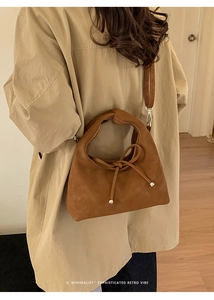 Detail of brown suede shoulder bag with a bow drawstring and metal tip accents
