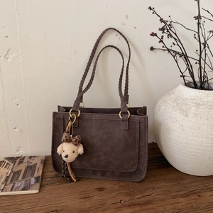 Detail of dark brown tote bag with woven shoulder straps and plush puppy charm accessory