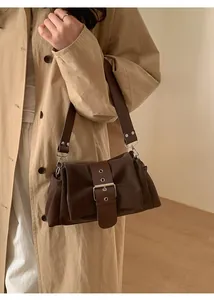 Détail d'un sac bandoulière marron foncé avec boucle à œillets porté sur trench beige