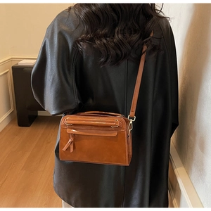 Détail d'un sac bandoulière marron caramel en similicuir avec pompons longs et boucles dorées