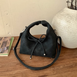 Detail of black suede handbag with bow tie and silver beads on a wooden desk
