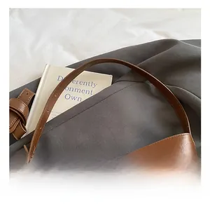 Detail of wide comfortable handle on vintage dark brown leather bucket bag over grey suit