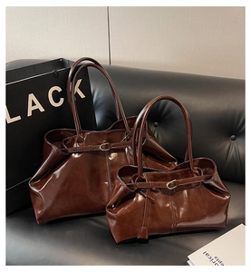 Detail of two dark brown vintage oil wax leather tote bags on a black leather sofa