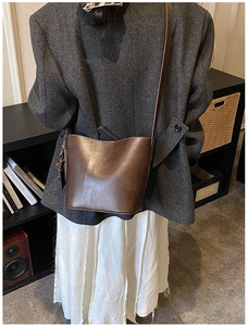 Deep brown bucket bag with leather texture worn by a model in a retro interior setting
