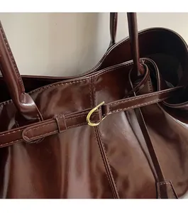 Detail of dark brown glossy leather tote bag showing fine stitching and gold D-ring hardware