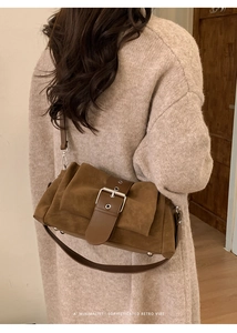 Détail d'un sac bandoulière en daim marron avec grande boucle sur un pull beige