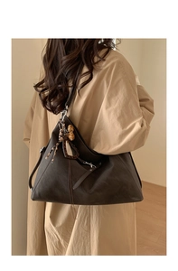 Détail du sac Hobo marron foncé avec breloque léopard et franges sur un manteau beige