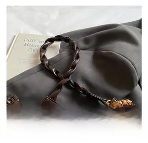 Detail of dark brown leather handbag with woven handle and vintage wooden bead tassel