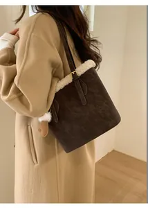 Detail of a brown suede bucket bag with faux fur trim worn with a beige wool coat
