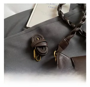 Detail of dark brown matte leather bag with golden buckles and woven strap on gray blazer