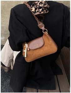 Detail of brown suede crossbody bag with vintage beaded charm and metal logo accent