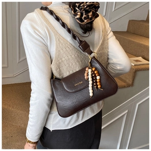 Detail of dark brown leather shoulder bag with woven strap and beaded tassel pendant