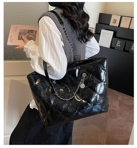 Detail of black quilted tote bag featuring glossy texture and metallic chain strap