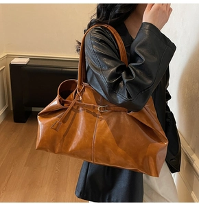 Caramel brown leather tote bag with metallic buckle shown in a stylish side view on shoulder