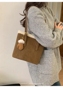 Close-up of brown suede tote bag featuring white faux fur trim and heart plush charm