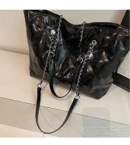 Detail of quilted black patent leather tote bag with silver metal chain strap