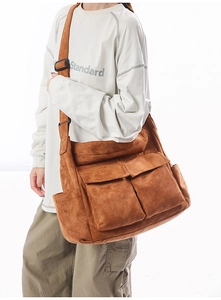Detail of a brown suede large capacity messenger bag with two front flap pockets