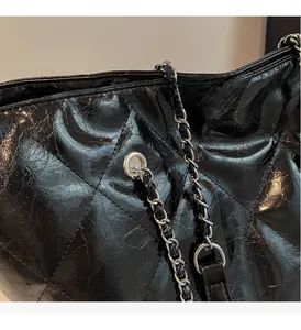 Close-up of quilted black leather texture with glossy finish and silver chain on tote bag