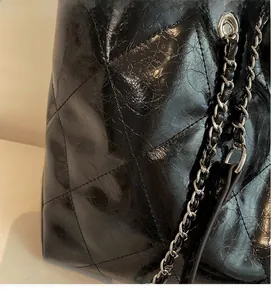 Close-up of black quilted glossy patent leather texture and silver metal chain strap