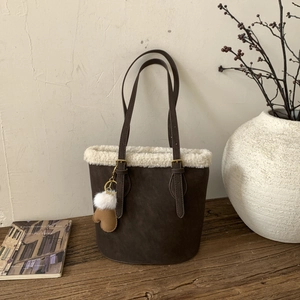 Detail of dark brown suede bucket bag with white faux shearling trim and glove charm