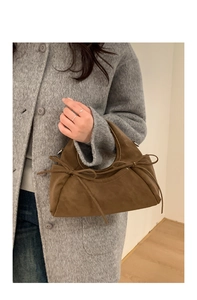 Détail d'un sac dumpling en daim marron avec nœuds élégants et poignées métalliques rondes