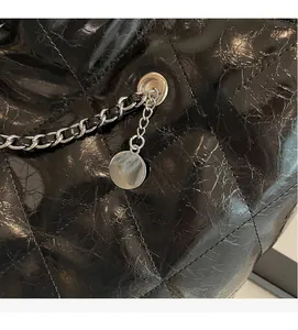 Close-up of quilted black leather tote bag with silver chain and circular charm detail
