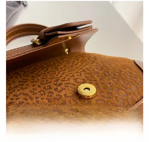 Macro detail of golden magnetic buckle on brown leather bag with leopard print texture