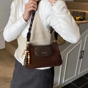 Détail d'un sac en daim marron avec bandoulière tressée et perles décoratives en bois naturel