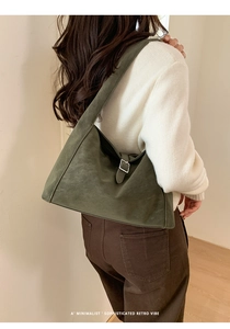 Detail of a dark green retro tote bag with silver buckle worn by a model in a minimal setting