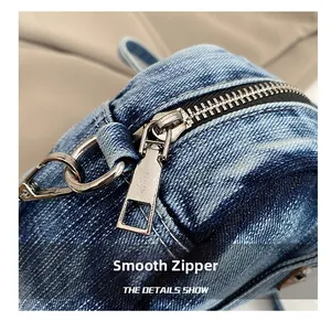 Close-up of smooth silver metal zipper on distressed blue denim handbag with quality stitching