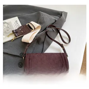 Detail of dark burgundy suede saddle bag with interchangeable wide woven shoulder strap