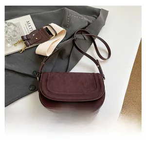 Detail of burgundy suede saddle bag with parallel stitching and two swappable shoulder straps