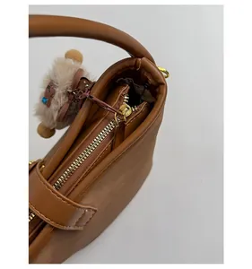 Detail of smooth gold zipper and plush bear charm on a brown faux leather bucket bag