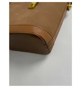 Macro shot of precise stitching and gold metal hardware on a brown suede handbag