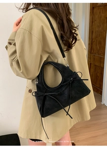 Détail du sac à main noir mat avec nœud et bandoulière amovible porté sur un trench