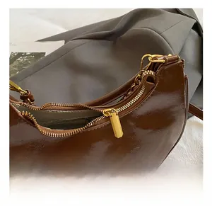 Detail of dark brown crinkled patent leather handbag with golden chain and zip