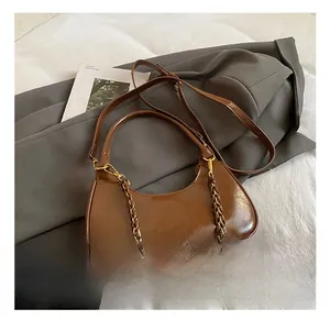 Brown faux leather crescent bag with metallic chain strap detail on soft bedding