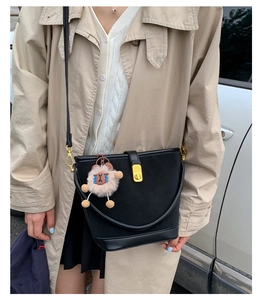 Close-up of a minimalist black bucket bag with a gold lock and a cute lamb charm