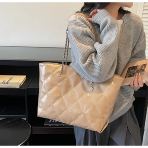Detail of beige quilted shoulder bag with silver chain strap and metal pendant charm