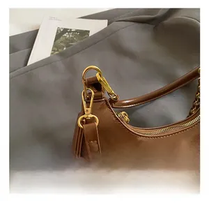 Detail of a brown oil-wax leather shoulder bag with polished gold metal hook and zipper