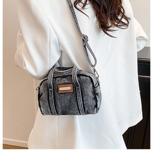 Detail of gray washed denim crossbody bag featuring a brown leather patch and retro style