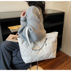 Detail of white quilted tote bag with metallic chain and elegant diamond stitch pattern