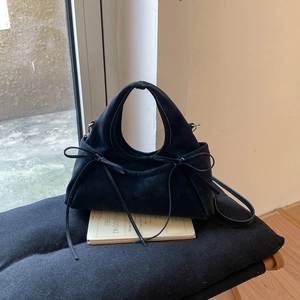 Détail d'un sac à main noir mat avec nœud posé sur des livres anciens avec lumière douce