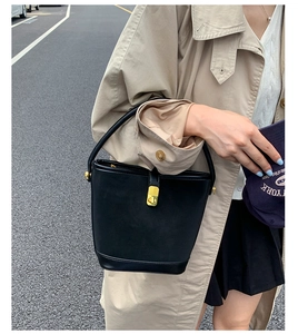 Detail of a black leather bucket bag featuring a matte finish and gold twist-lock closure