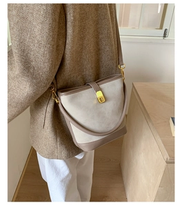 Close-up of beige bucket bag with gold twist lock and adjustable crossbody strap