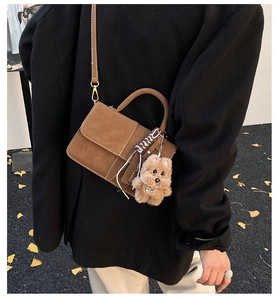 Detail of brown matte handbag with woven edge, plush puppy charm and metal buckle accent